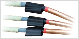 Three prepared medium-voltage cable cores side by side: pale insulation at the rear, a short black stress control tube recovered over each screen step, a red band ahead of it and bare stranded copper conductor at the front
